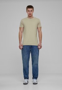 Beige bomulds t-shirt med rund hals, parret med slidte blå denim jeans og hvide sneakers. Enkel, afslappet pasform med korte ærmer.