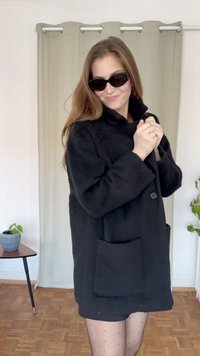 Μαύρο υπερμεγέθες παλτό από μαλακό ύφασμα με ψηλό γιακά, κλείσιμο με κουμπιά μπροστά και μεγάλη πατίνα. Φοριέται με μαύρα γυαλιά ηλίου.