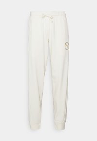 Krämfärgade sweatpants med elastisk dragsko i midjan, muddar vid anklarna och en liten gold Puma-logotyp med cirkulär text på övre vänstra lår.