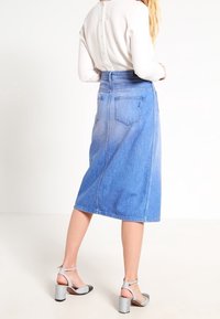 Jupe midi en denim avec une taille haute, dégradé bleu, deux poches arrière et une coupe droite. Associée à des sandales à talons blocs grises.