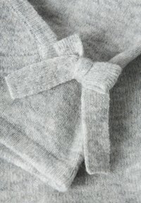 Tessuto a maglia grigio chiaro morbido con un piccolo fiocco annodato, che mostra la texture e le cuciture su un indumento piegato.