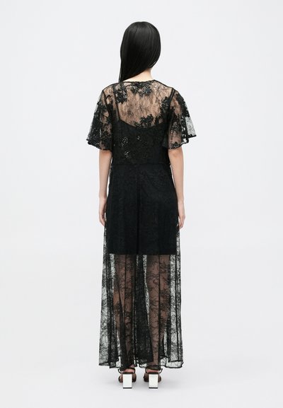 Juoda nėriniuota suknelė su permatomu sluoksniu, trumpomis rankovėmis ir prigludusia liemene. Audinys puošia gėlių raštais ir turi laisvą siluetą.