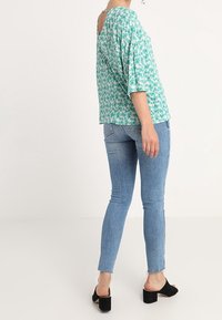 Lässiges türkisfarbenes Hemd mit floralem Muster, V-Ausschnitt und Dreiviertelärmeln, kombiniert mit hellblauen Skinny-Jeans und schwarzen High Heels.