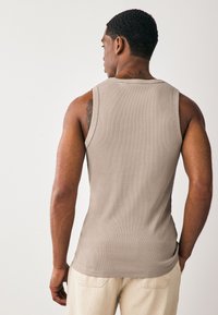 Débardeur beige côtelé avec une coupe ajustée, des bretelles fines et une texture lisse. Vue de dos, mettant en valeur les détails des épaules et du haut des bras.