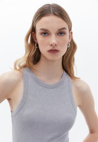Šedý žebrovaný top s kulatým výstřihem a širokými ramínky. Tkanina vypadá měkce a má přiléhavý siluetu.