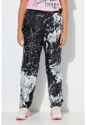 Persoon draagt zwart-witte broek met abstract patroon, elastische taille en boorden, roze en witte sneakers en een roze top.