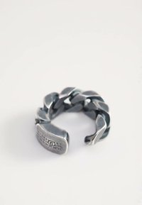 Grubia srebrna obrączka z łańcuchem metalowym z otwartym końcem i małymi wygrawerowanymi cyframi w pobliżu otworu na białym tle.