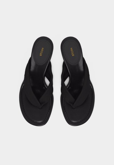 Pár čiernych šmykľavých sandálov s širokými skrútenými látkovými remienkami a plochými podrážkami, zobrazený zhora na svetlom pozadí.