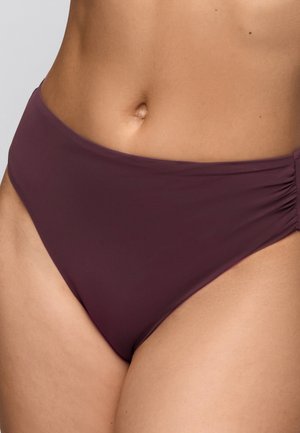 Middenstuk van een vrouw die hooggetailleerde donkerpaarse bikinibroekjes met geplooide zijkanten draagt tegen een effen achtergrond.