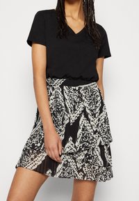 Top negro con escote en V combinado con una falda de capas que presenta un estampado floral y geométrico en blanco y negro, con texturas transparentes y plisadas.