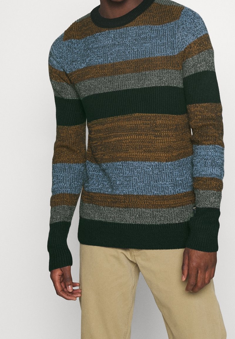 Pull en maille avec des rayures horizontales bleu, marron, gris et vert. Col rond et poignets côtelés. Le tissu présente une texture apparente.