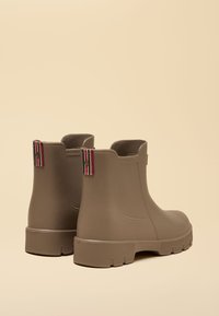 Pair of matte taupe ankle rain boots with chunky ridged soles and red-white-black striped pull tabs at the back.