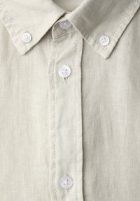 Beige linen button-down shirt with a pointed collar and white four-hole buttons fastened along the front.