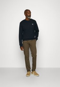 Námornícky sveter s logom na hrudi, skombinovaný s úzkymi béžovými nohavicami a béžovými teniskami. Pohodlný, neformálny outfit.