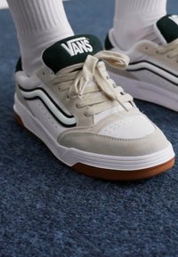 Vans tenisice s bež i bijelom gornjom površinom, zelenim akcentima, crnim prugama i teksturiranom gumenom potplatom. Čipke su bež.