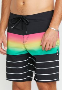 Un short de bain noir avec un motif dégradé passant du rose au vert, accentué par des rayures horizontales blanches et une taille avec cordon de serrage.