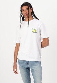 Hvid bomulds t-shirt med korte ærmer, der har et farverigt citronmotiv og teksten "Limón Citrico" på venstre bryst.