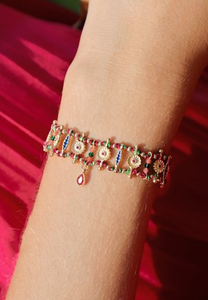 Bracelet doré avec des perles colorées, des accents floraux et un pendentif en forme de goutte. Présente un travail du métal complexe et des détails semblables à des bijoux.