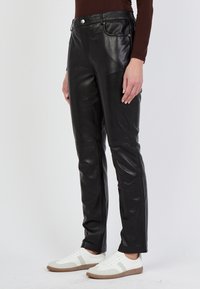 Zwarte leren broek met een slim fit ontwerp, voorzien van een ritssluiting en vijf zakken. Gladde afwerking met zichtbare stiksels.