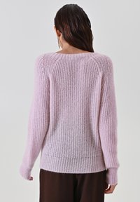 Maglione lavorato a maglia rosa chiaro con un motivo a onde testurizzato, maniche lunghe e scollo rotondo, con un orlo leggermente sagomato.