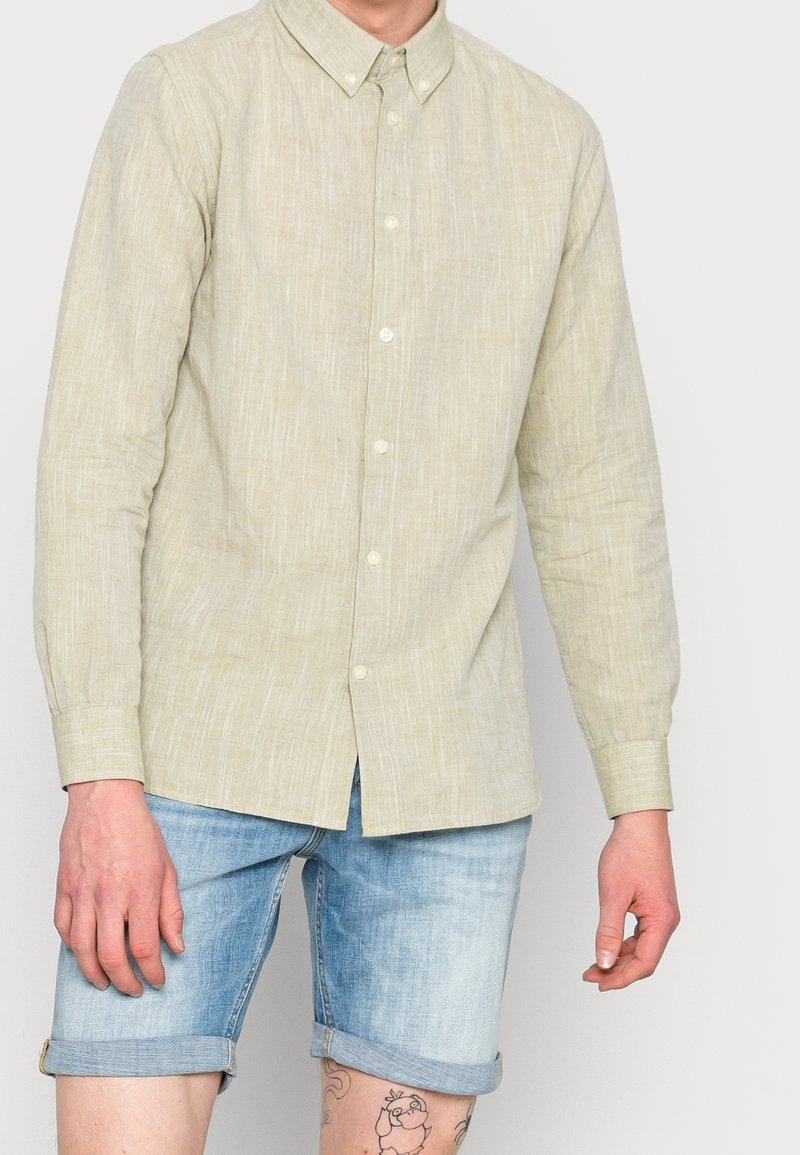 Vaaleanvihreä, teksturoidusta kankaasta valmistettu napitettava paita, jossa on kauluskäänne ja pitkät hihat, yhdistettynä käännettyihin farkkushortseihin.