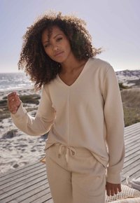 Maglione a coste beige con scollo a V e maniche rilassate, abbinato a pantaloni con coulisse dello stesso colore. Tessuto morbido e vestibilità casual.