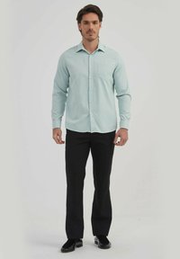 Chemise boutonnière bleu clair avec une poche poitrine, manches longues et texture lisse, associée à un pantalon noir et des chaussures.