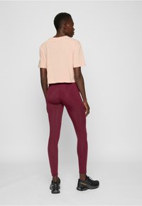 Lys rosa t-skjorte med korte ermer, kombinert med høytlivede vinrøde leggings og svarte joggesko. Enkel design, avslappet passform.