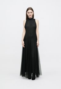 Black sleeveless maxi dress with a high neck, sheer tulle overlay, and soft texture. Floor-length with a flowing silhouette and subtle detailing.