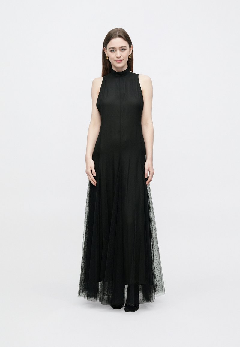 Black sleeveless maxi dress with a high neck, sheer tulle overlay, and soft texture. Floor-length with a flowing silhouette and subtle detailing.
