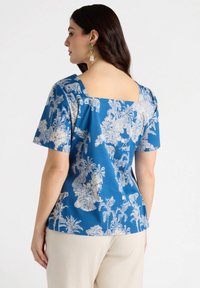 Blue short-sleeve top featuring a square back neckline, with a white tropical pattern and textured fabric. Accented with visible stitching details.