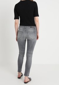 Top negro ajustado y acanalado de manga corta, combinado con jeans de mezclilla gris de tiro medio. Los jeans cuentan con bolsillos traseros y un ligero desvanecimiento. Sandalias planas negras.