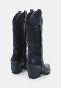 Černé kožené kovbojské boty s vysokými holeněmi, složitým prošíváním připomínajícím listy, bočním zipem a klínovými podpatky. Hladký povrch.