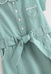 Groen-wit geruit jurkje met korte mouwen, knoopsluiting, een zak en een strikceintuur. Gemaakt van lichtgewicht stof met een gestructureerd detail.