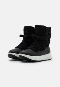 Bottes noires à la cheville avec une tige en textile doux, dotées de lacets épais et d'une semelle blanche contrastante, conçues pour la chaleur et le confort.