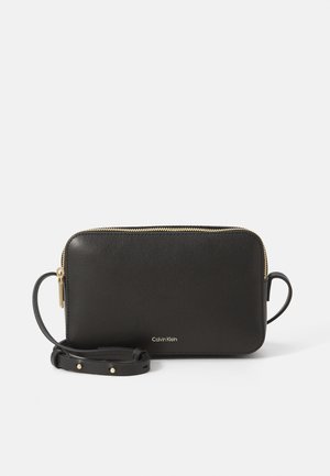 Schwarze rechteckige Leder-Umhängetasche mit goldenem Reißverschluss und verstellbarem Riemen, kleines Calvin Klein-Logo in Gold vorne in der Mitte.