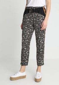 Zwarte bloemenprint broek met een zwarte tailleband, trekkoord en zijaccenten. Gecombineerd met witte platform sneakers.
