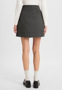 Grauer Wollminirock mit tailliertem Bund, seitlichen Taschen und ausgestelltem Schnitt, kombiniert mit schwarzen Lackslippers und cremefarbenen Socken.