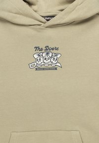 Felpa khaki con cappuccio, caratterizzata da una grafica frontale di tre teschi con dei cappelli e uno slogan. Tessuto morbido con tasca a marsupio frontale.