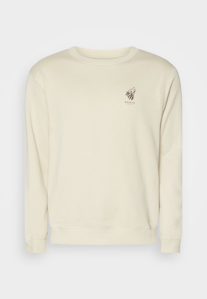 Sweatshirt bege com mangas longas, punhos canelados e gola redonda. Apresenta uma pequena gráfica de um leão castanho e texto no peito. Textura de tecido macio.