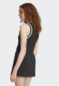Robe noire sans manches avec un corsage ajusté et une jupe évasée, présentant des accents blancs sur le décolleté. Tissu en coton doux, design décontracté.
