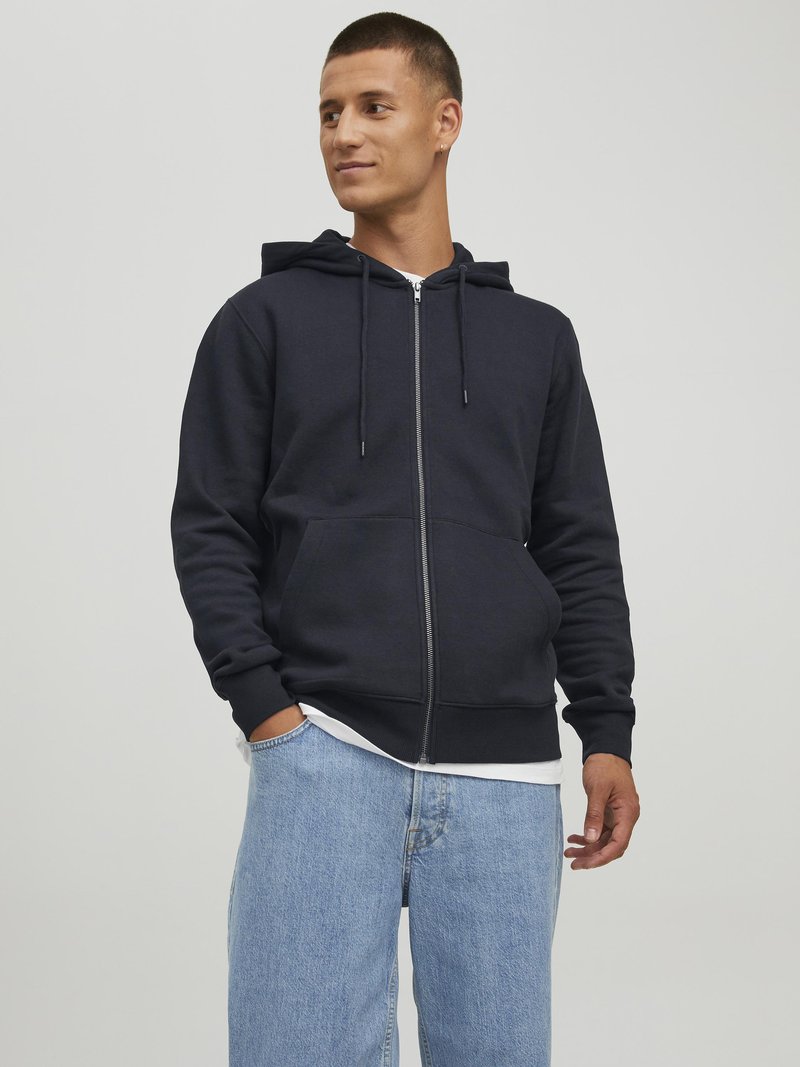 Navy-blaues Zip-Hoodie aus weichem Material mit Kängurutasche, verstellbarem Kordelzug an der Kapuze, gerippten Bündchen, getragen über einem weißen Shirt und hellblauen Jeans.