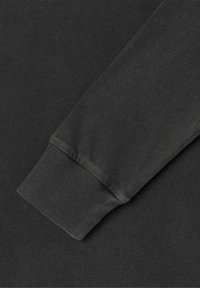 Mörkgrå långärmad ärm lagd diagonalt över en matchande mörkgrå tygbakgrund, vilket visar ribbad textur och sömdetaljer.