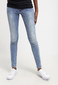 Kapeetit farkut vaaleansinisenä denimissä, joissa on häivytetty pesu, minimaalinen ommel ja viisi taskua, yhdistettynä valkoisiin tennareihin.