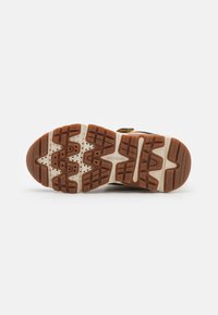 Semelle de chaussure de sport marron et blanche avec un motif de semelle, composée de matériaux en caoutchouc et en plastique, conçue pour l'adhérence et la durabilité.
