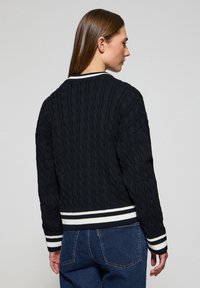 Svart kabelstickad tröja med kort design, vitrandig ribbad fåll och manschetter, med rund halsringning och texturerad detaljering.