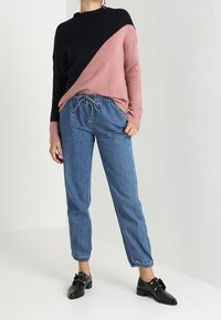 Chunky stickad tröja i navy och rosa med en asymmetrisk design; blå tapered byxor med elastiska manschetter; svarta loafers med spännhandtag.