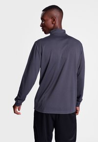 Mörkgrå långärmad tröja med hög krage och strukturerad tyg. Har en avslappnad passform och förlängda ärmar. Bakifrån visad.