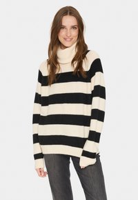 Schwarz- und cremefarbener gestreifter Rollkragenpullover mit einer weichen, strukturierten Oberfläche. Er verfügt über lange Ärmel und eine lockere Passform. Kombiniert mit dunklen Jeans.