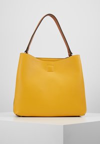 Bolso tote de cuero amarillo con un acabado texturizado, que presenta un solo asa marrón y un detalle cuadrado en el frente.